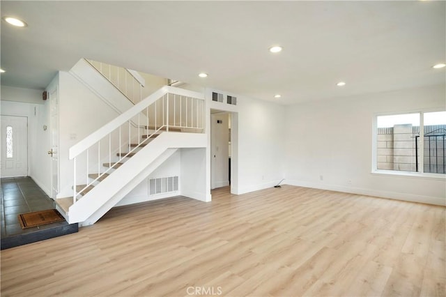 unfurnished living room featuring stairway, plenty of natural light, wood finished floors, and visible vents