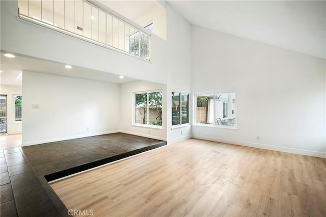 unfurnished living room featuring wood finished floors, baseboards, and high vaulted ceiling