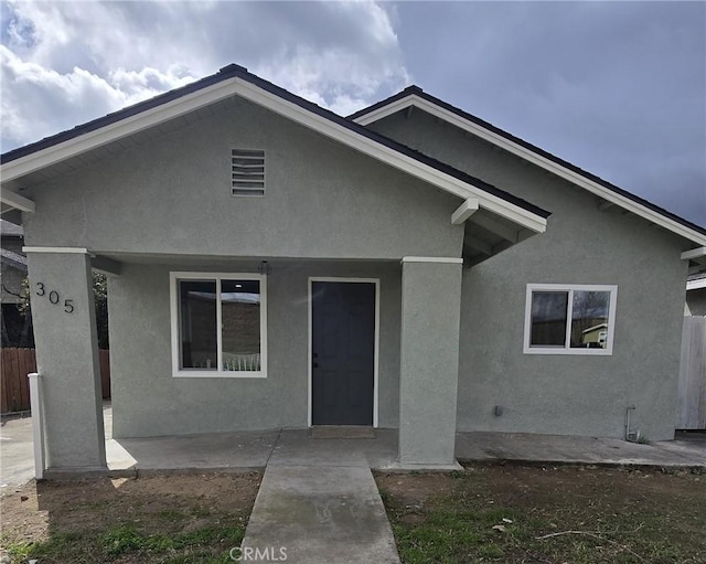 view of front of house with a patio area, fence, and stucco siding