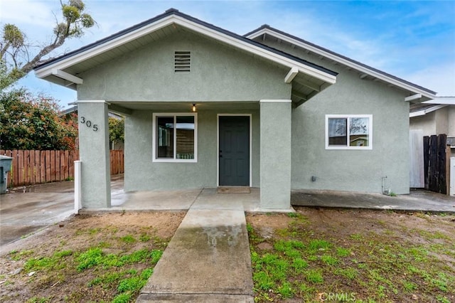 bungalow featuring a porch, stucco siding, and fence