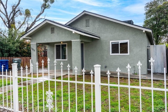 bungalow featuring stucco siding, fence, and a front lawn