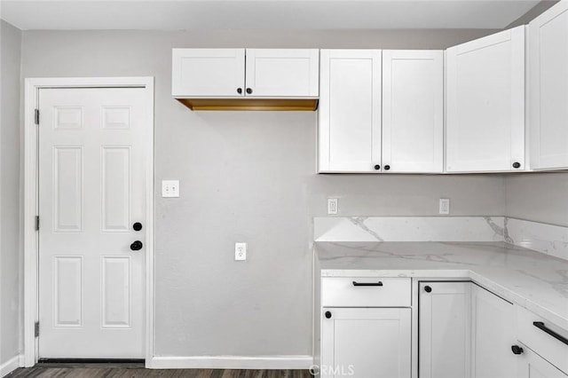kitchen featuring white cabinetry, dark wood-style flooring, baseboards, and light stone counters