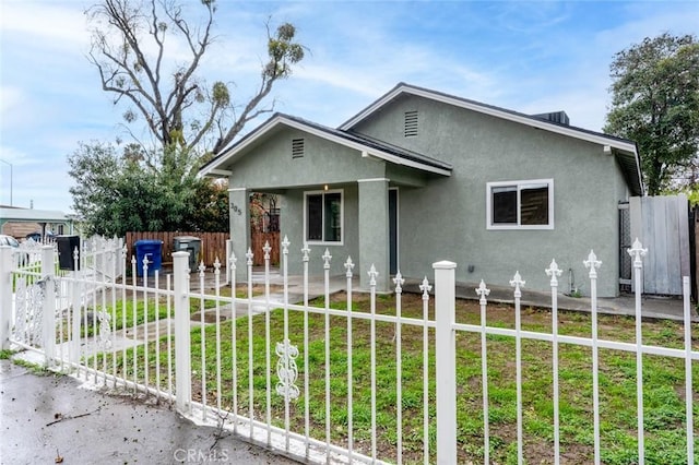 bungalow featuring a front lawn, stucco siding, and fence