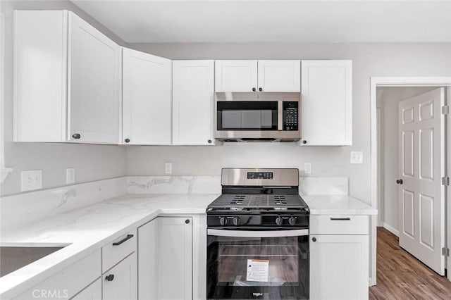 kitchen featuring stainless steel appliances, a sink, light wood finished floors, white cabinets, and light stone countertops