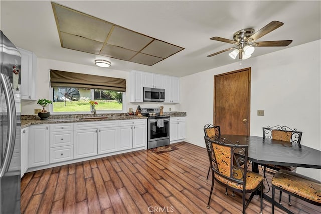 kitchen featuring a sink, stone countertops, dark wood finished floors, appliances with stainless steel finishes, and white cabinets