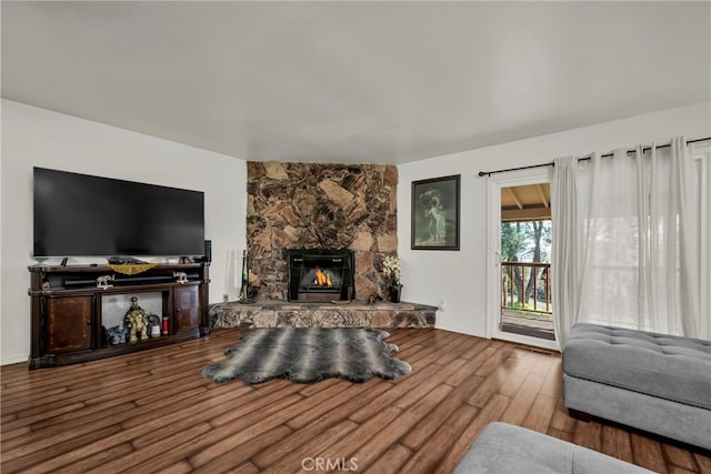 living room with a stone fireplace and wood finished floors