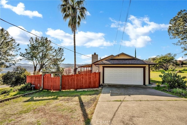 exterior space featuring fence, an attached garage, a chimney, concrete driveway, and a lawn