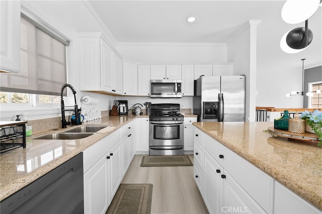 kitchen featuring light wood finished floors, a sink, ornamental molding, stainless steel appliances, and white cabinets