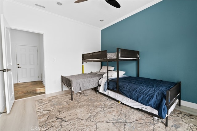 bedroom with a ceiling fan, wood finished floors, visible vents, baseboards, and crown molding