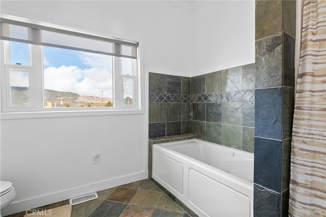 full bathroom featuring visible vents, baseboards, toilet, a bath, and stone finish floor