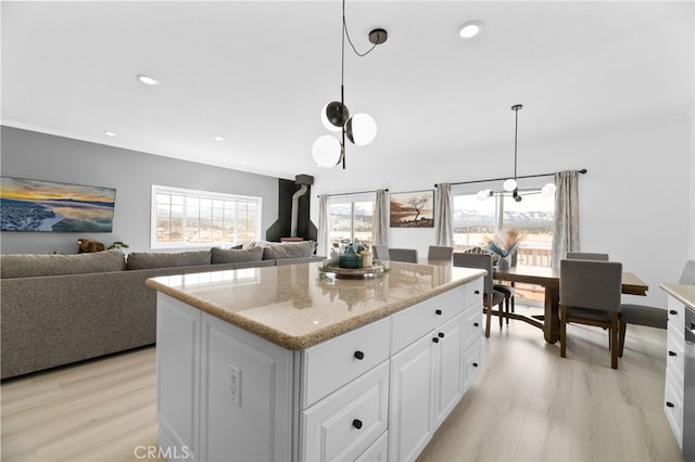 kitchen featuring white cabinets, light stone countertops, light wood-type flooring, and pendant lighting