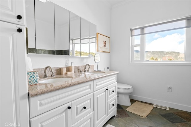 bathroom featuring double vanity, toilet, baseboards, and a sink