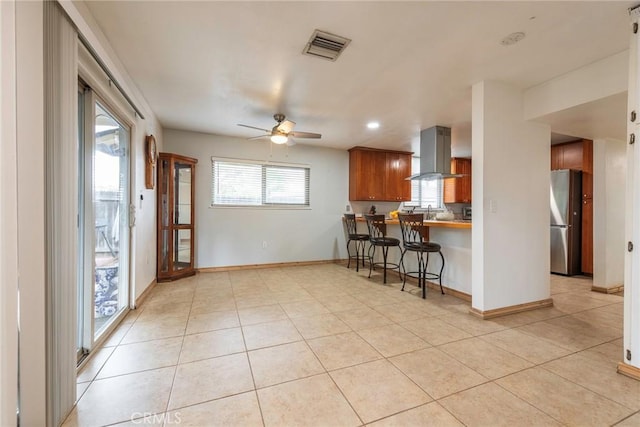 kitchen with visible vents, extractor fan, a kitchen bar, light tile patterned floors, and freestanding refrigerator