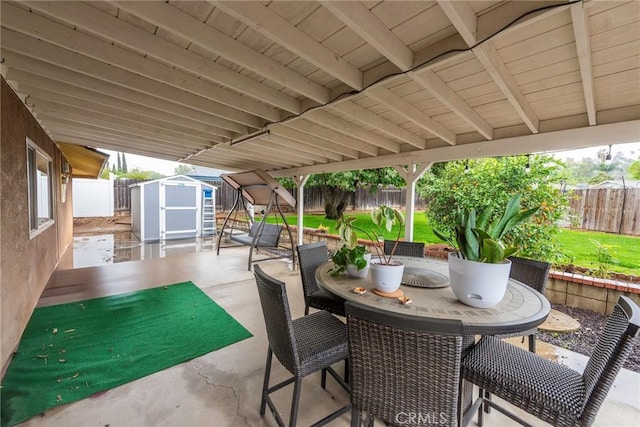 view of patio featuring a storage unit, an outbuilding, outdoor dining area, and a fenced backyard