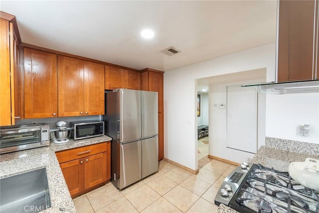 kitchen featuring visible vents, brown cabinets, a sink, freestanding refrigerator, and gas stove