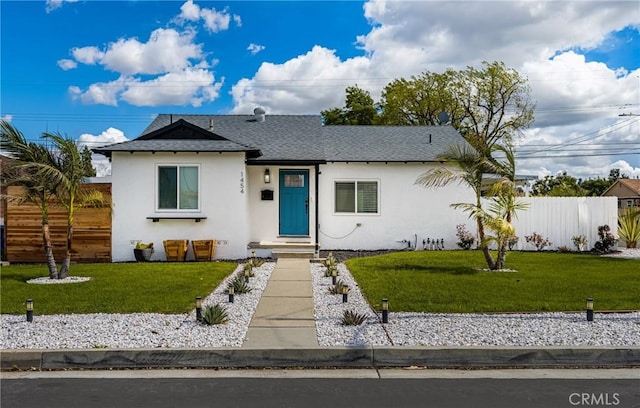 view of front of property with stucco siding, a shingled roof, a front lawn, and fence