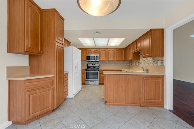 kitchen featuring light countertops, decorative backsplash, appliances with stainless steel finishes, a peninsula, and brown cabinetry