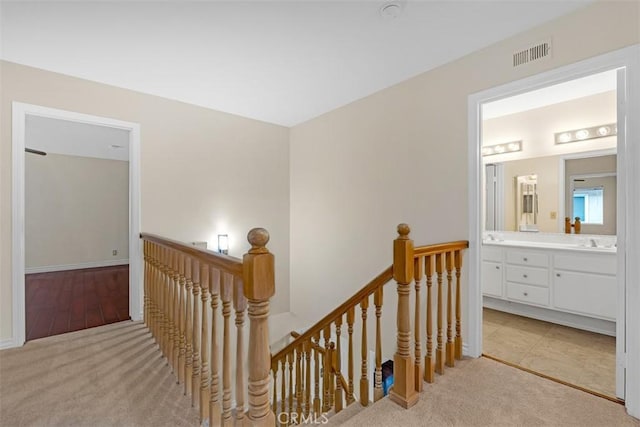 corridor with an upstairs landing, visible vents, a sink, and carpet floors