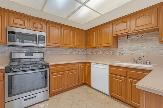 kitchen featuring a sink, stainless steel appliances, brown cabinetry, and light countertops