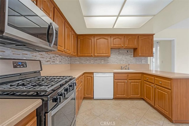 kitchen featuring brown cabinets, a sink, appliances with stainless steel finishes, light countertops, and decorative backsplash