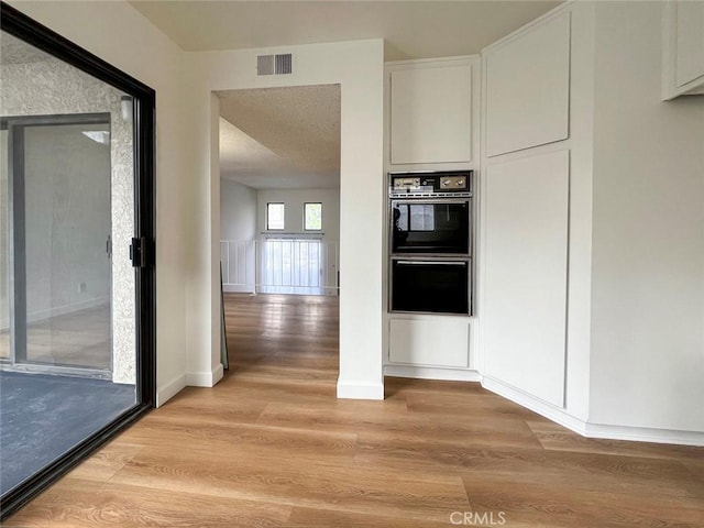 interior space with visible vents, white cabinets, dobule oven black, and light wood finished floors