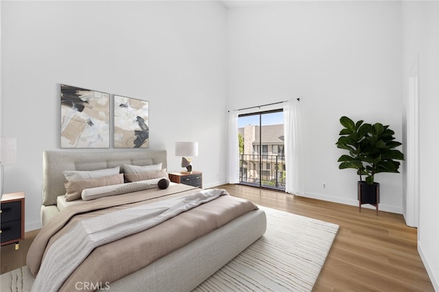 bedroom featuring light wood-type flooring, baseboards, a towering ceiling, and access to outside