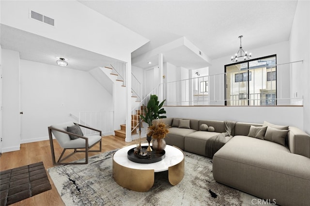 living area featuring a chandelier, visible vents, stairway, and wood finished floors