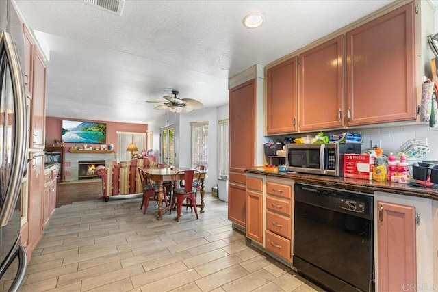 kitchen with light wood finished floors, visible vents, ceiling fan, a warm lit fireplace, and appliances with stainless steel finishes