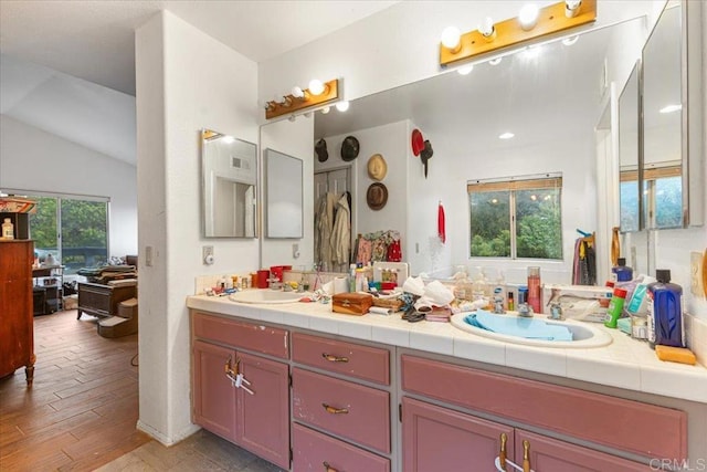 full bathroom with double vanity, vaulted ceiling, wood finished floors, and a sink