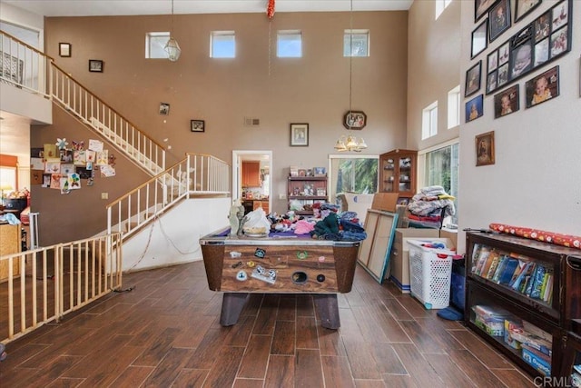 living room featuring visible vents, wood finish floors, an inviting chandelier, a high ceiling, and stairs