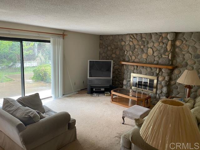 living room featuring a textured ceiling, a stone fireplace, and carpet flooring