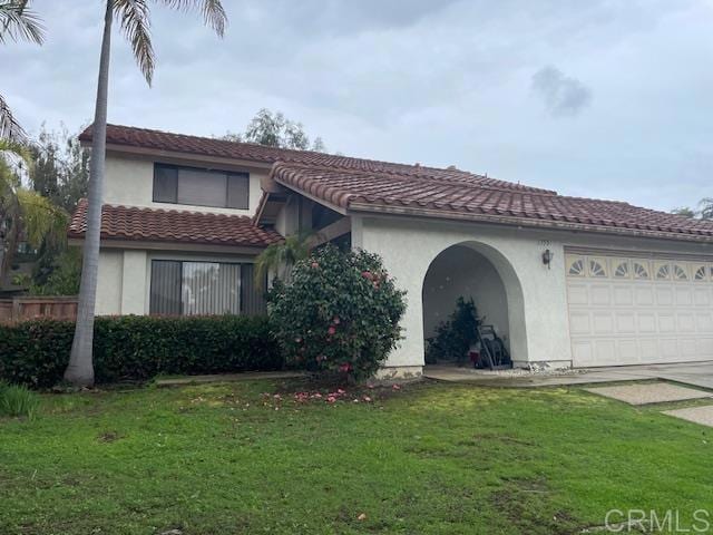 mediterranean / spanish house with an attached garage, stucco siding, concrete driveway, a front lawn, and a tile roof