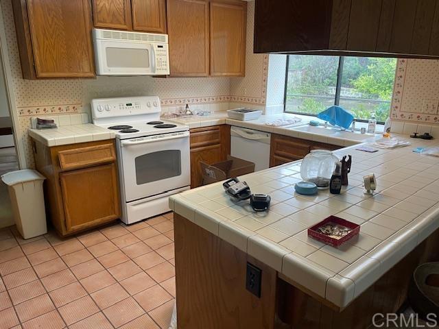 kitchen with tasteful backsplash, tile countertops, white appliances, light tile patterned flooring, and wallpapered walls