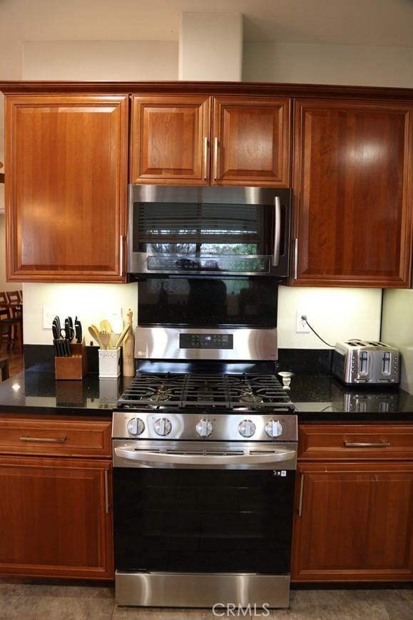 kitchen with dark stone countertops, brown cabinetry, and appliances with stainless steel finishes