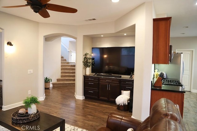 living room featuring visible vents, a ceiling fan, dark wood finished floors, stairway, and arched walkways