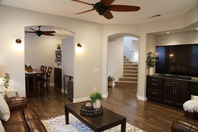 living room with arched walkways, visible vents, a ceiling fan, and dark wood-style floors