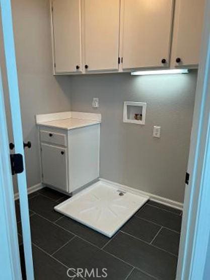 clothes washing area featuring cabinet space, hookup for a washing machine, baseboards, and dark tile patterned floors