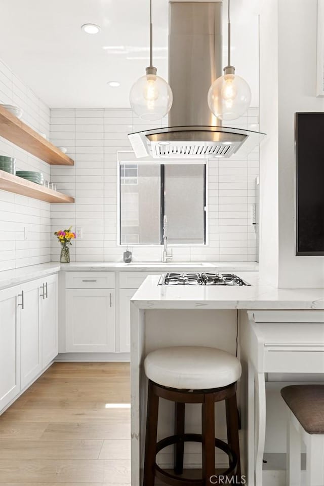 kitchen with light wood-style flooring, island exhaust hood, a kitchen breakfast bar, backsplash, and light countertops