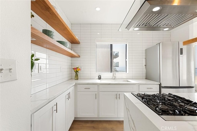 kitchen with open shelves, wall chimney range hood, freestanding refrigerator, white cabinetry, and a sink