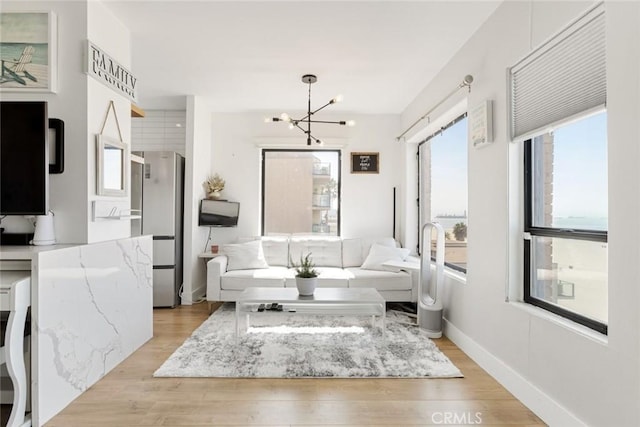 living room featuring an inviting chandelier, light wood-style flooring, and baseboards