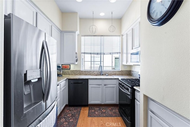 kitchen featuring light wood-style flooring, a sink, black appliances, white cabinets, and decorative light fixtures