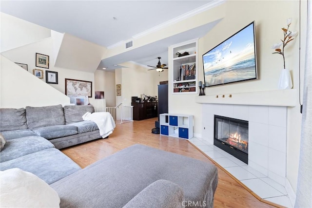 living area featuring visible vents, ornamental molding, wood finished floors, a fireplace, and ceiling fan