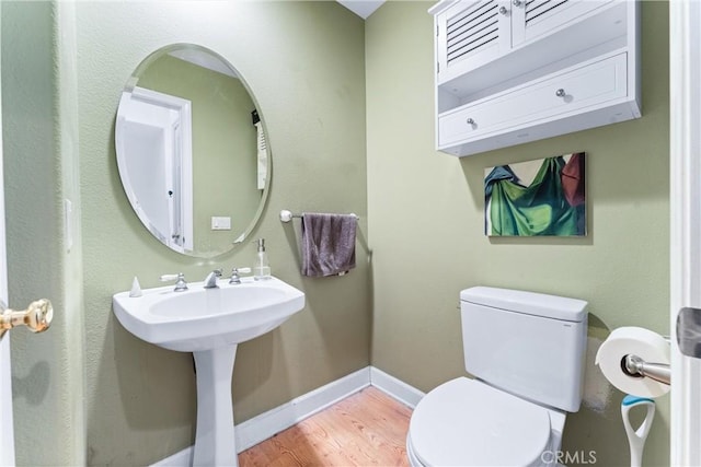 half bathroom with a sink, baseboards, toilet, and wood finished floors