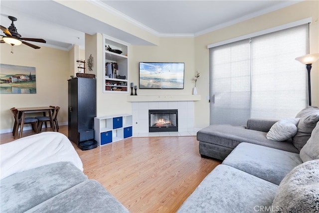 living room with ceiling fan, built in shelves, wood finished floors, and ornamental molding