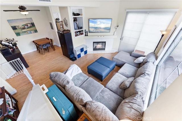 living room featuring built in shelves, wood finished floors, visible vents, a fireplace, and ceiling fan