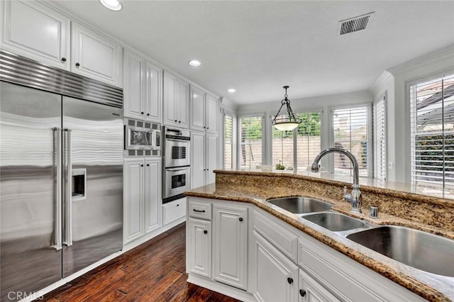 kitchen with visible vents, built in appliances, dark wood-style floors, white cabinetry, and a sink