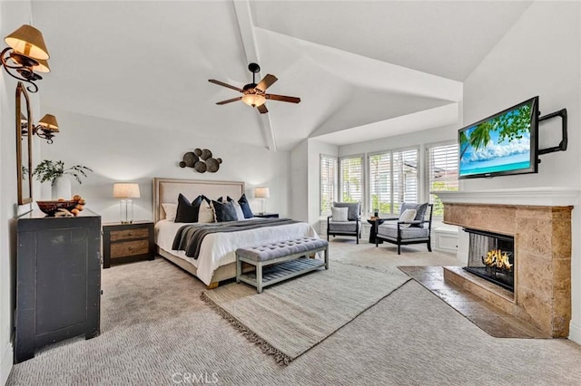 carpeted bedroom with a tiled fireplace, lofted ceiling with beams, and ceiling fan