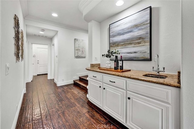 bar featuring dark wood-type flooring, baseboards, ornamental molding, indoor wet bar, and a sink