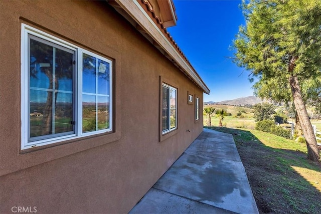 view of side of home featuring a patio area, a lawn, a mountain view, and stucco siding