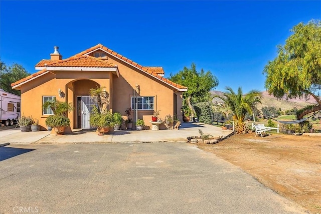 mediterranean / spanish-style house with a chimney, stucco siding, and a tile roof